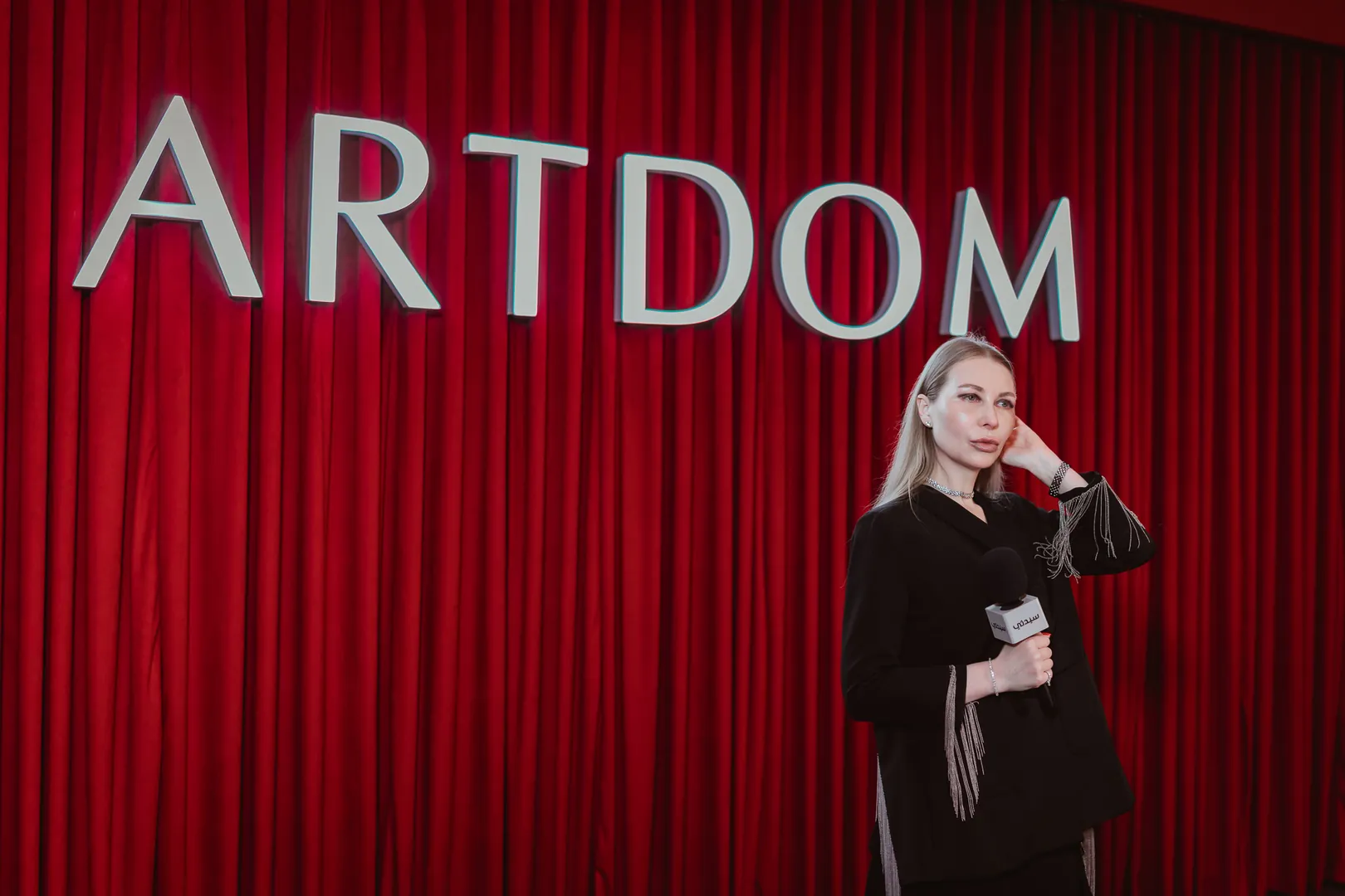 The host at the microphone before the red ARTDOM curtain