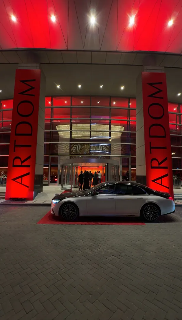 The entrance at night, a car drawn up between the red columns