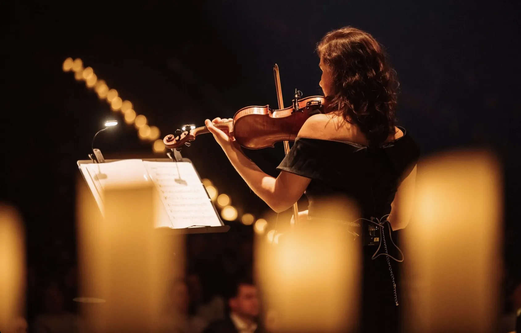 A violinist playing behind candles in the foreground