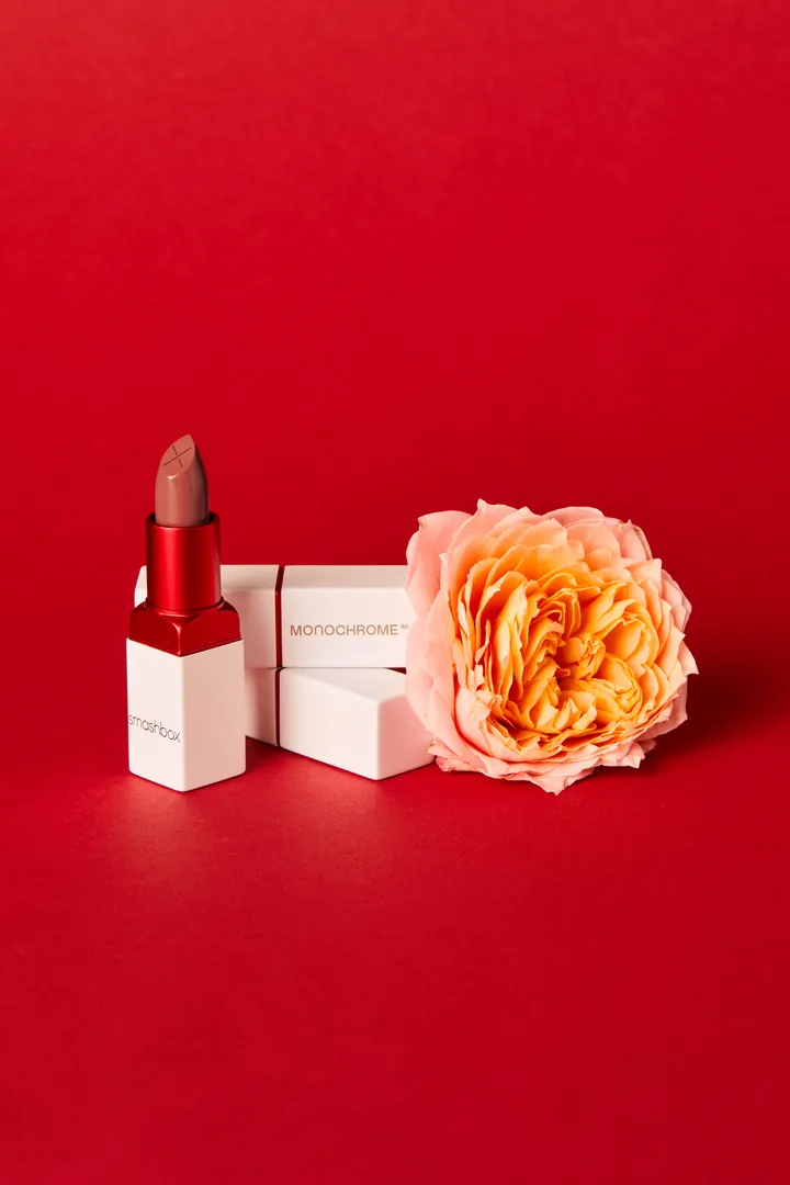 A lipstick beside a peach rose on red