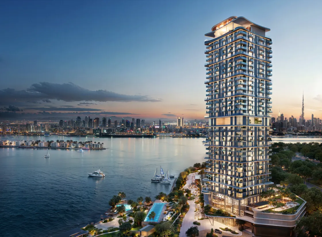 A residential tower at dusk over the water, the Dubai skyline behind