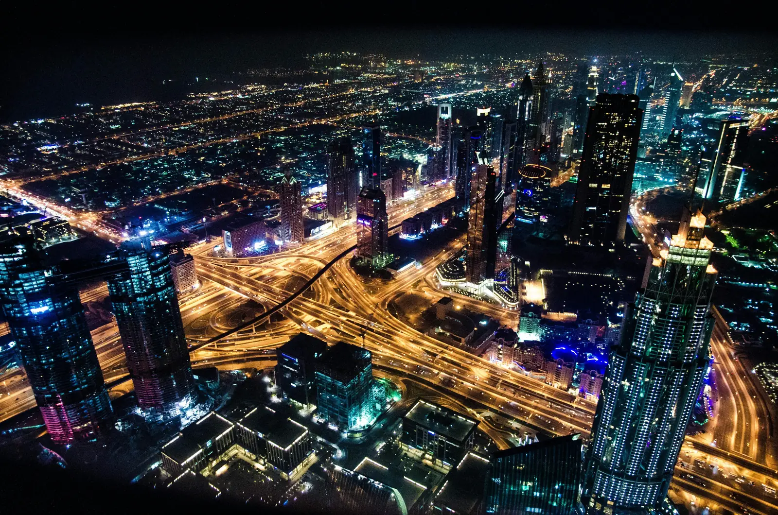 Dubai at night from high above: lit towers around a multi-level motorway interchange, with traffic running through it in lines of light.